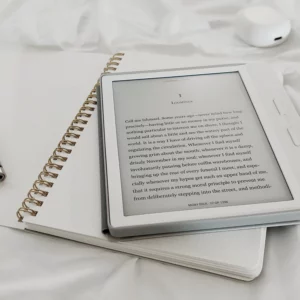 La photo représente un carnet d'écriture avec un stylo. Dessus est posée une liseuse blanche de la marque Kobo