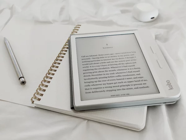 La photo représente un carnet d'écriture avec un stylo. Dessus est posée une liseuse blanche de la marque Kobo